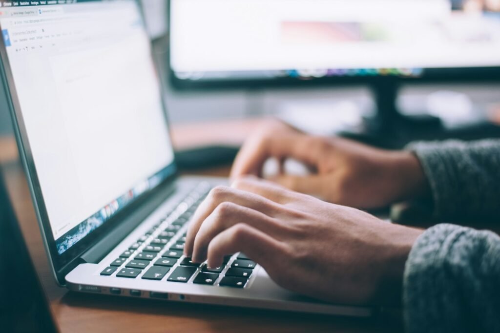 Person typing on a laptop at a wooden desk while drafting AI prompts for vibe coding