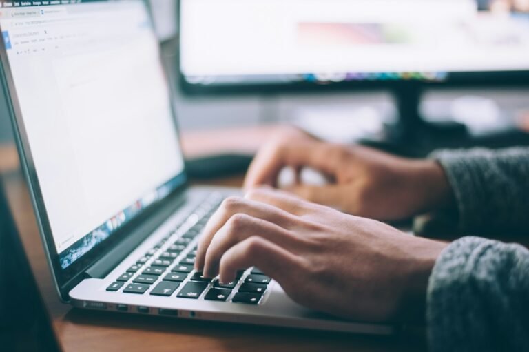 Person typing on a laptop at a wooden desk while drafting AI prompts for vibe coding